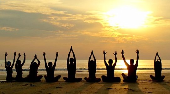 Group of people practicing yoga at sunset by the ocean